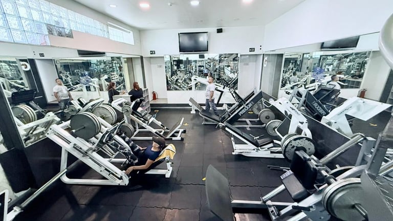 Modern gym interior with exercise machines, natural light from large windows, and people working out on cardio equipment
