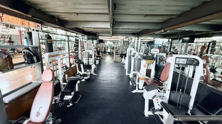 Interior of a modern gym with rows of exercise equipment and weight machines lining both sides of a black floor